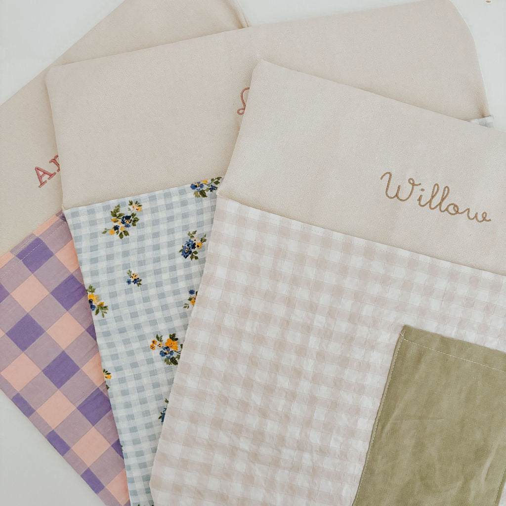Personalised chair bags in pink and purple gingham design, embroidered with names, perfect for kids' study areas.