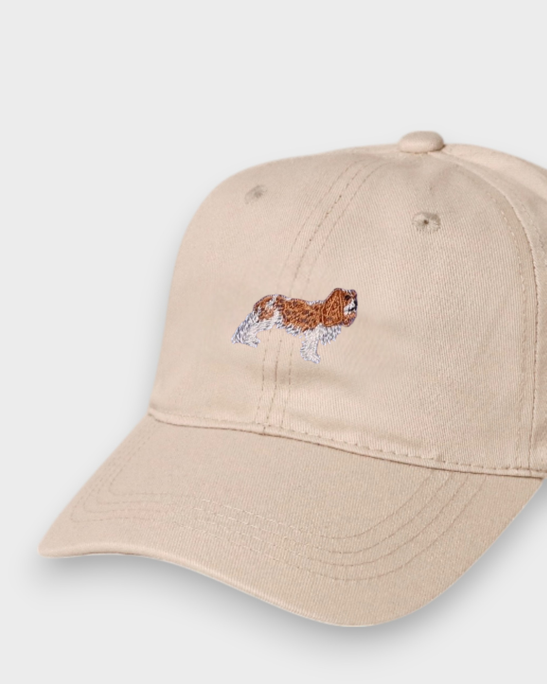 Beige baseball cap with embroidered King Charles Spaniel design and personalized embroidery option.