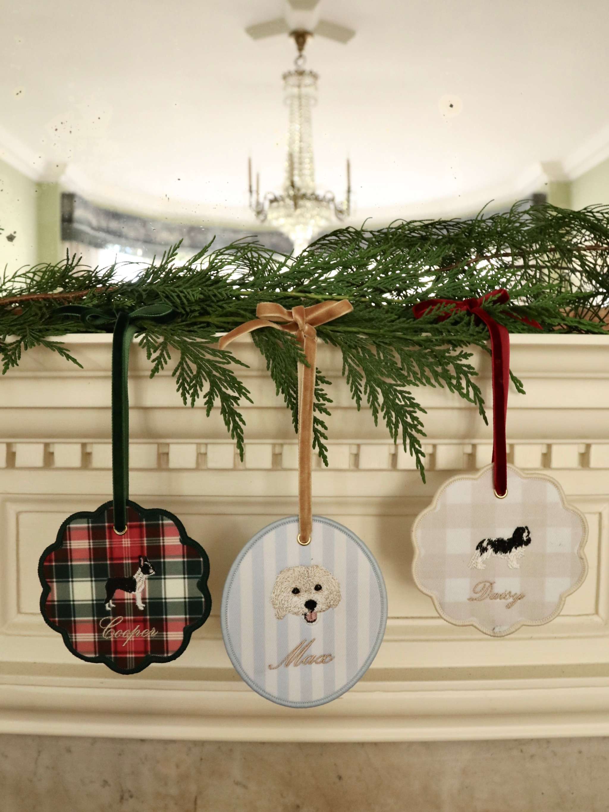 Custom pet ornaments with embroidered dog breeds and personalized names hanging with velvet ribbons on greenery decoration