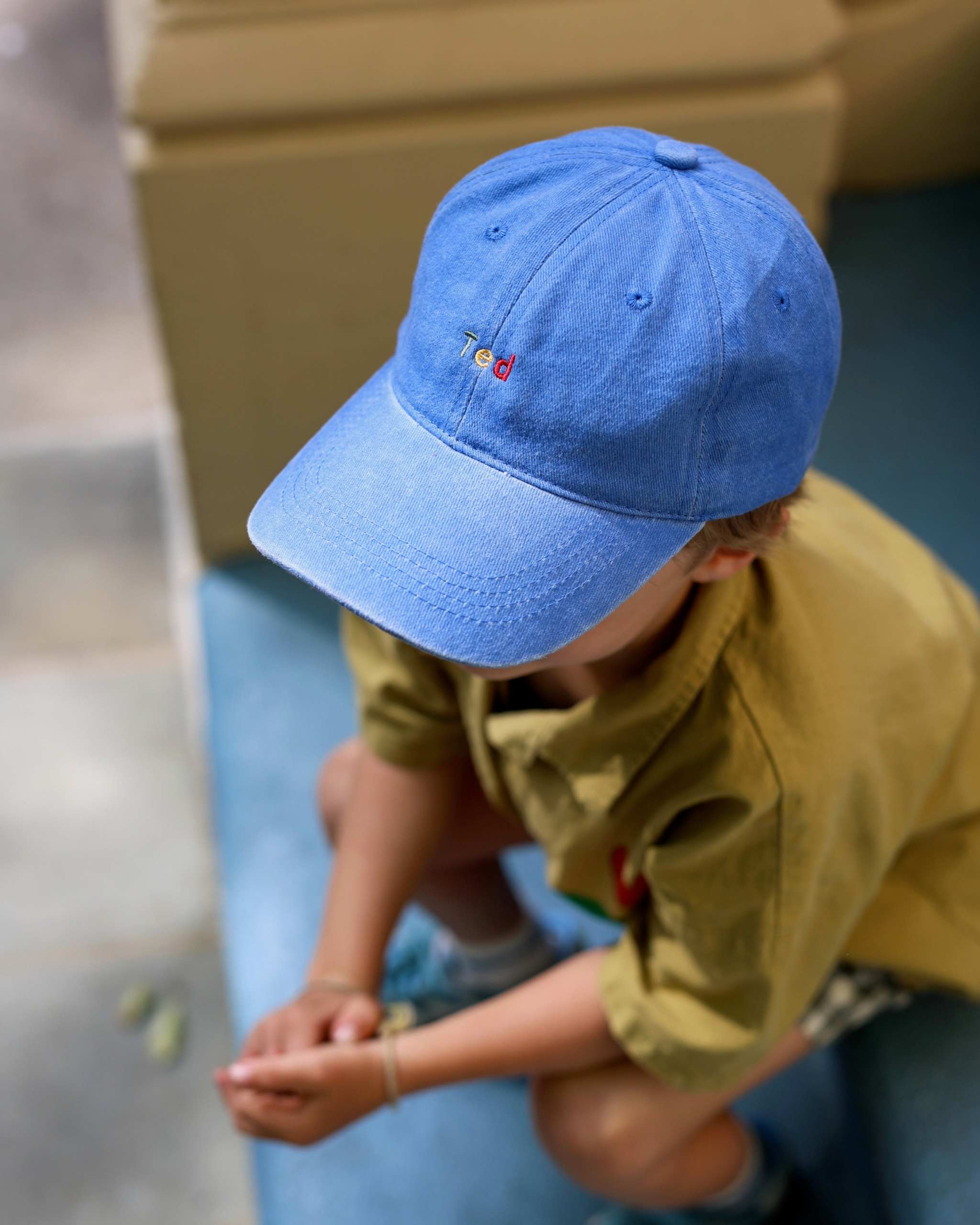 Blue personalised hat with multi-coloured text on a child outdoors.