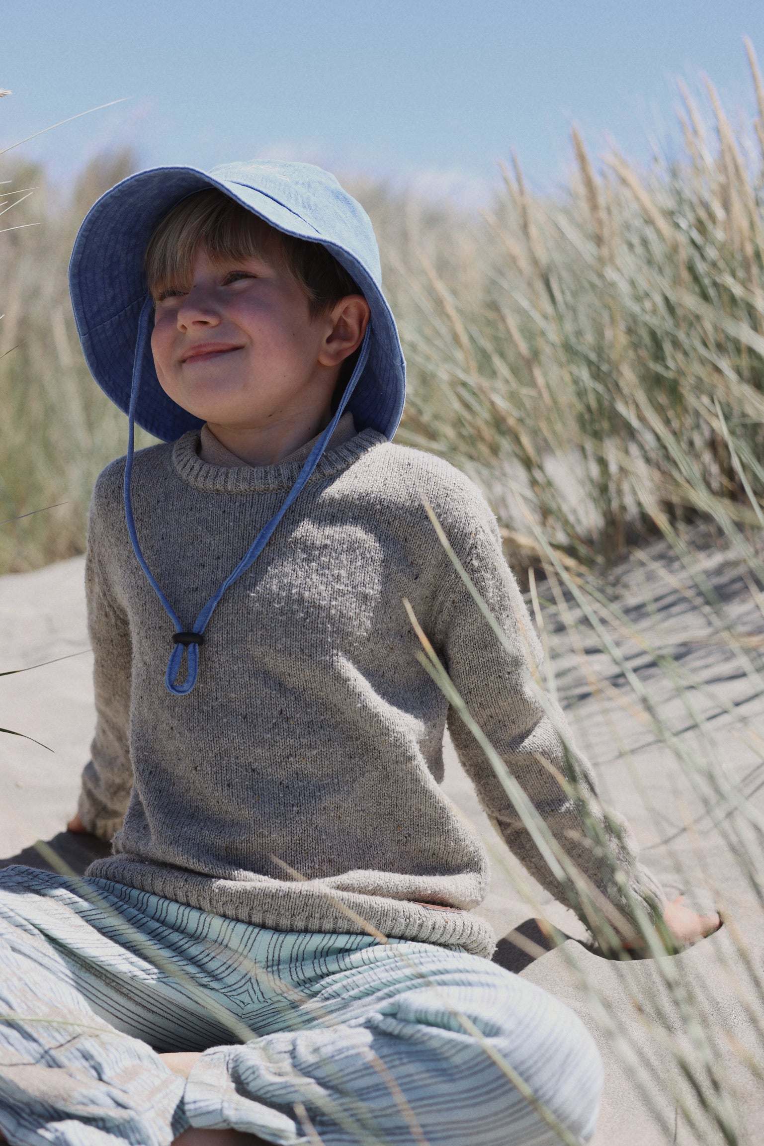 Child wearing a blue customised bucket hat made of 100% washed cotton at the beach.