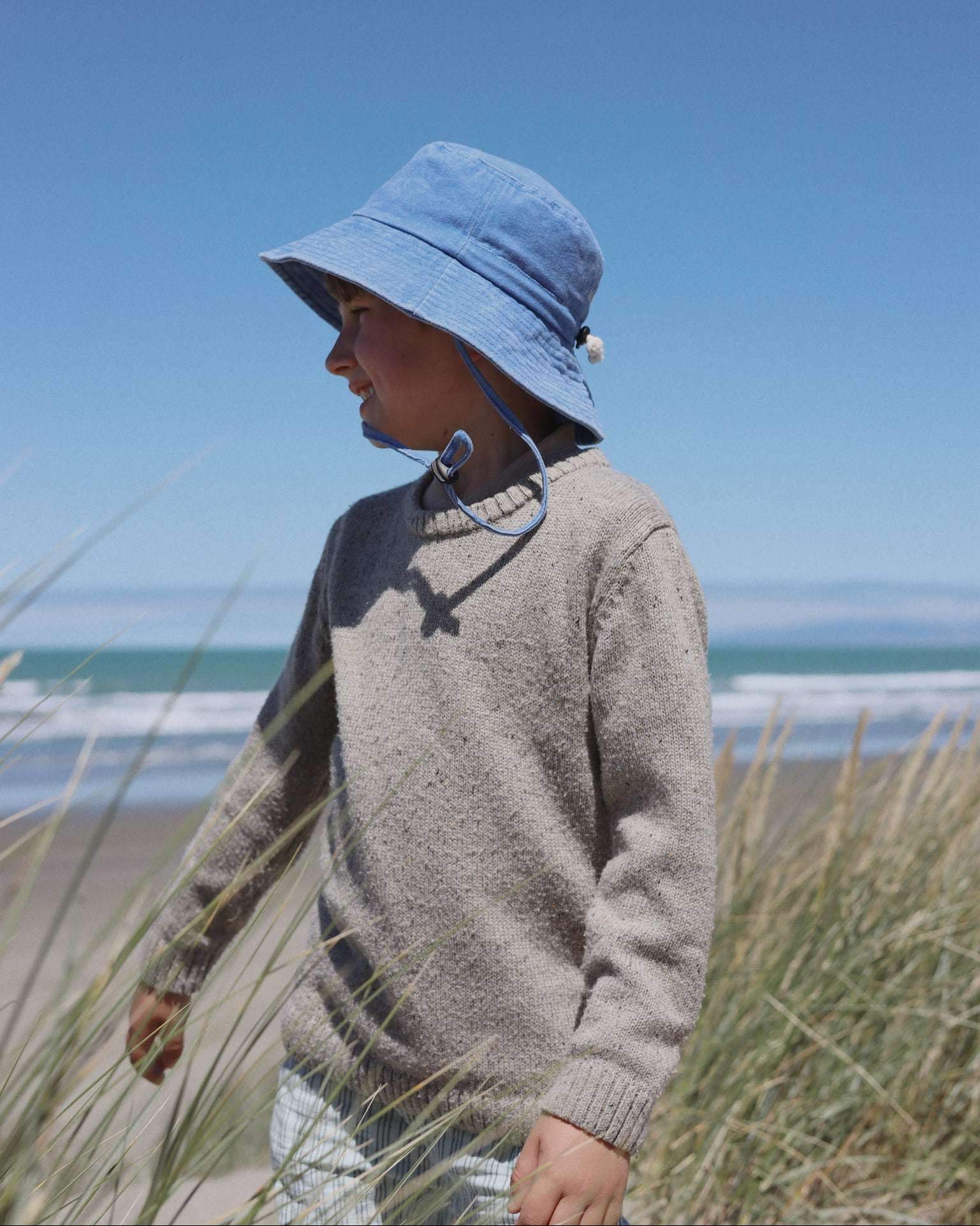 Child wearing a blue personalised bucket hat made of soft washed cotton by the beach