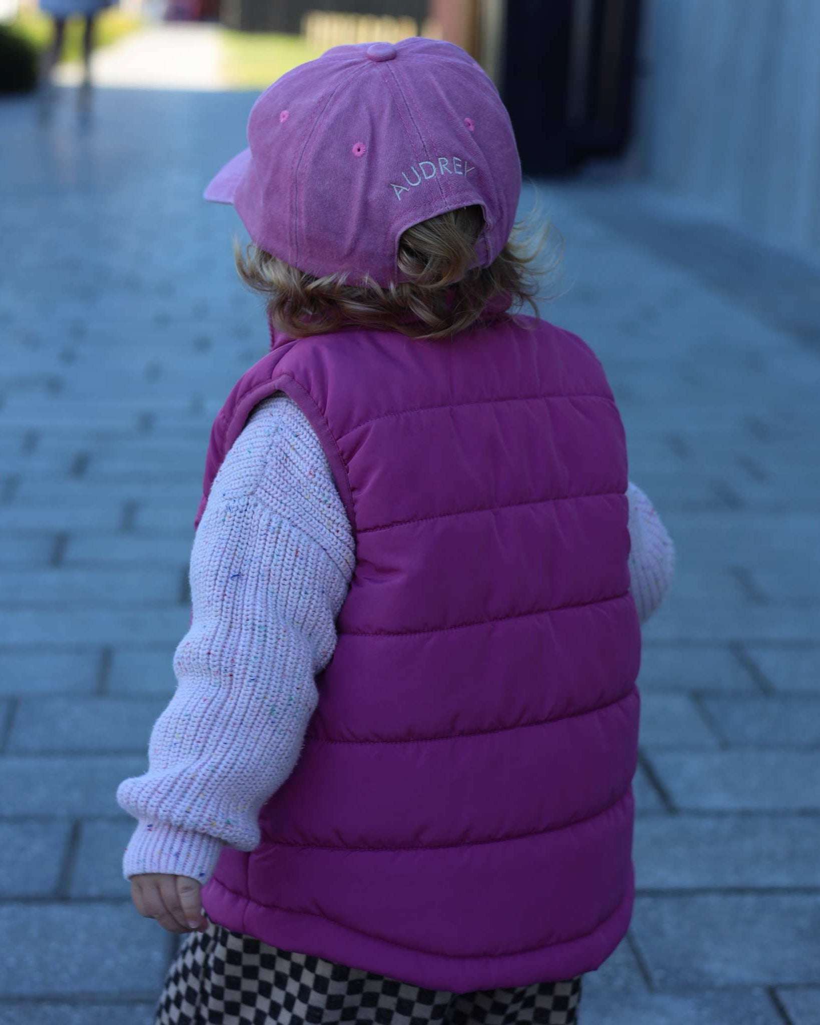 Child wearing a pink Greyhound/Whippet personalised hat with embroidered name on the back and matching pink padded vest outdoors
