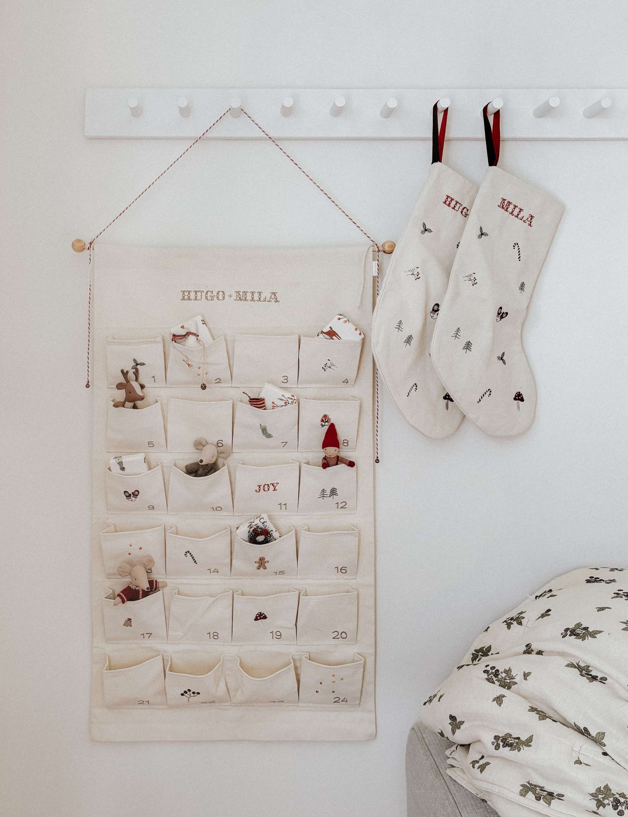Embroidered Advent Calendar with personalized names, ivory cotton canvas, decorative pockets, and hanging string with tiny bells.