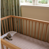 Merino baby blanket in a crib with wooden rails, showcasing soft, breathable wool.