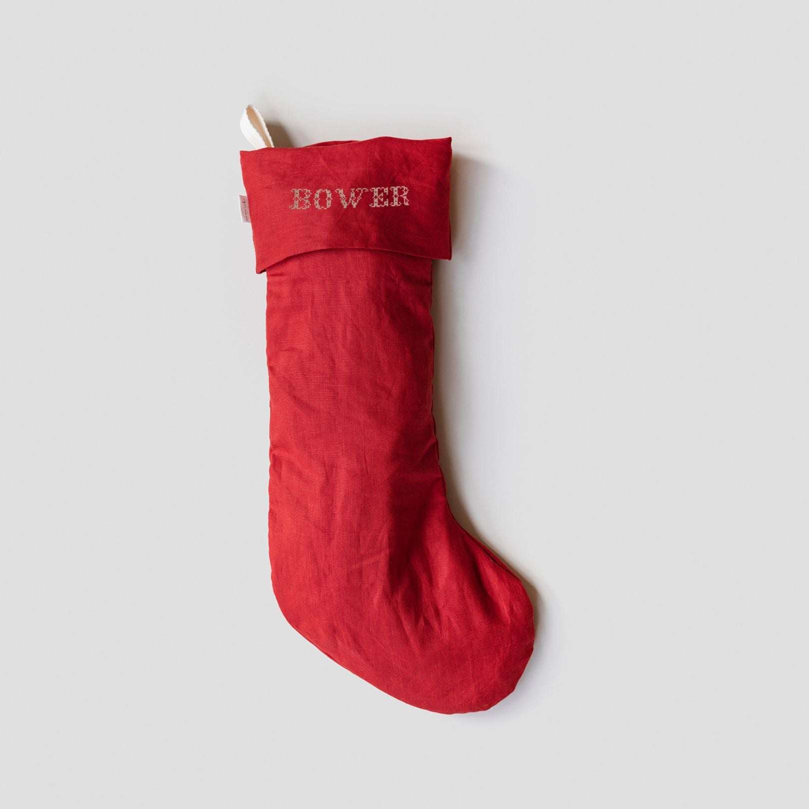 Red linen Christmas stocking with Nordic cross stitch name embroidery and cotton loop hanging on gray background
