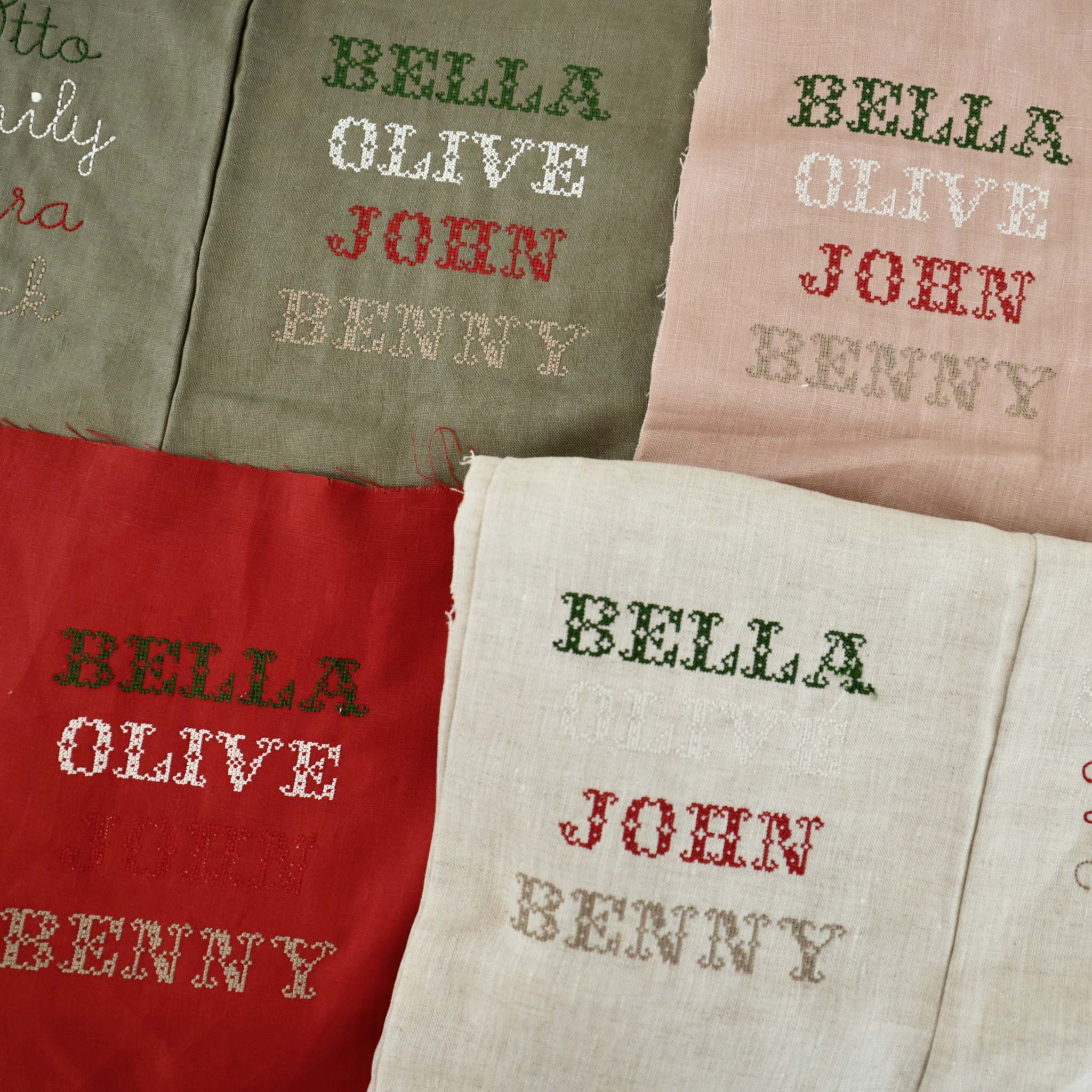 Set of personalized linen Christmas stockings in various colors with Nordic cross stitch names Bella, Olive, John, and Benny.