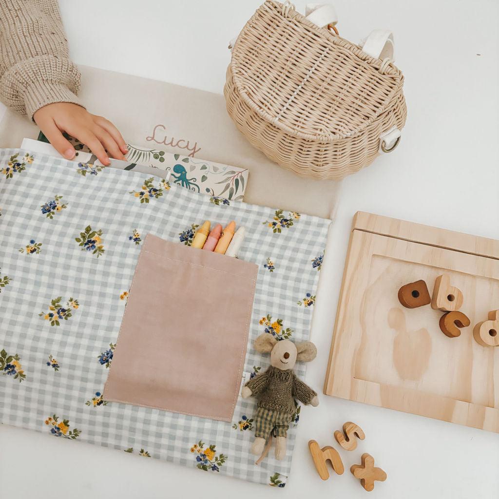 Personalised floral gingham chair bag with crayons and toys on a learning table.