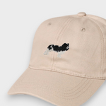 Beige baseball cap with embroidered black and white King Charles Spaniel design, personalized embroidery option on back, made from 100% washed cotton.
