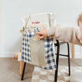 Personalised blue gingham chair bag on a child's chair, featuring embroidered name and front pocket for organization.