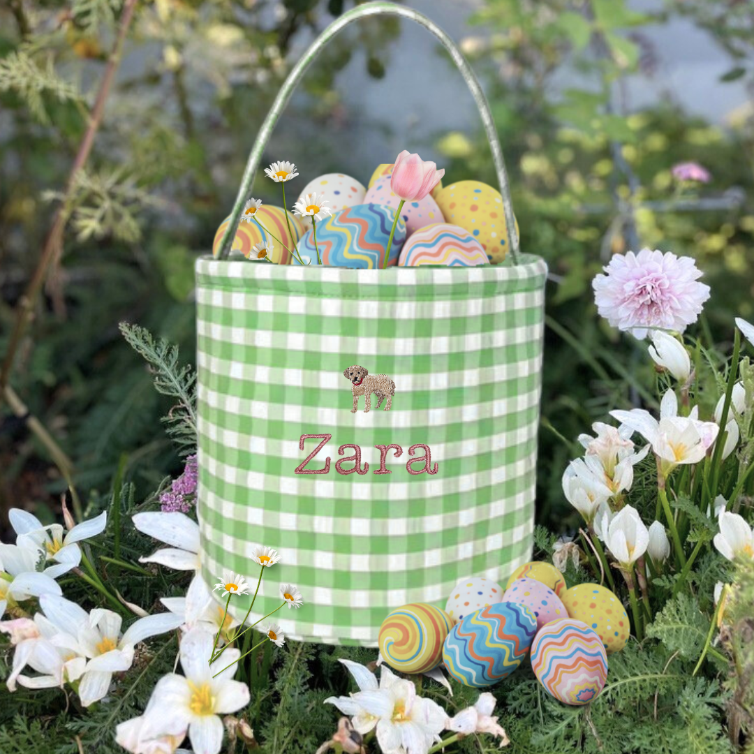Gingham personalised Easter bucket with embroidery, surrounded by flowers and colorful eggs.