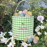 Gingham personalised Easter bucket with embroidery, surrounded by flowers and colorful eggs.