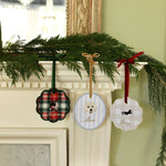 Festive personalized pet ornaments hanging on a decorated mantelpiece with greenery and ribbons