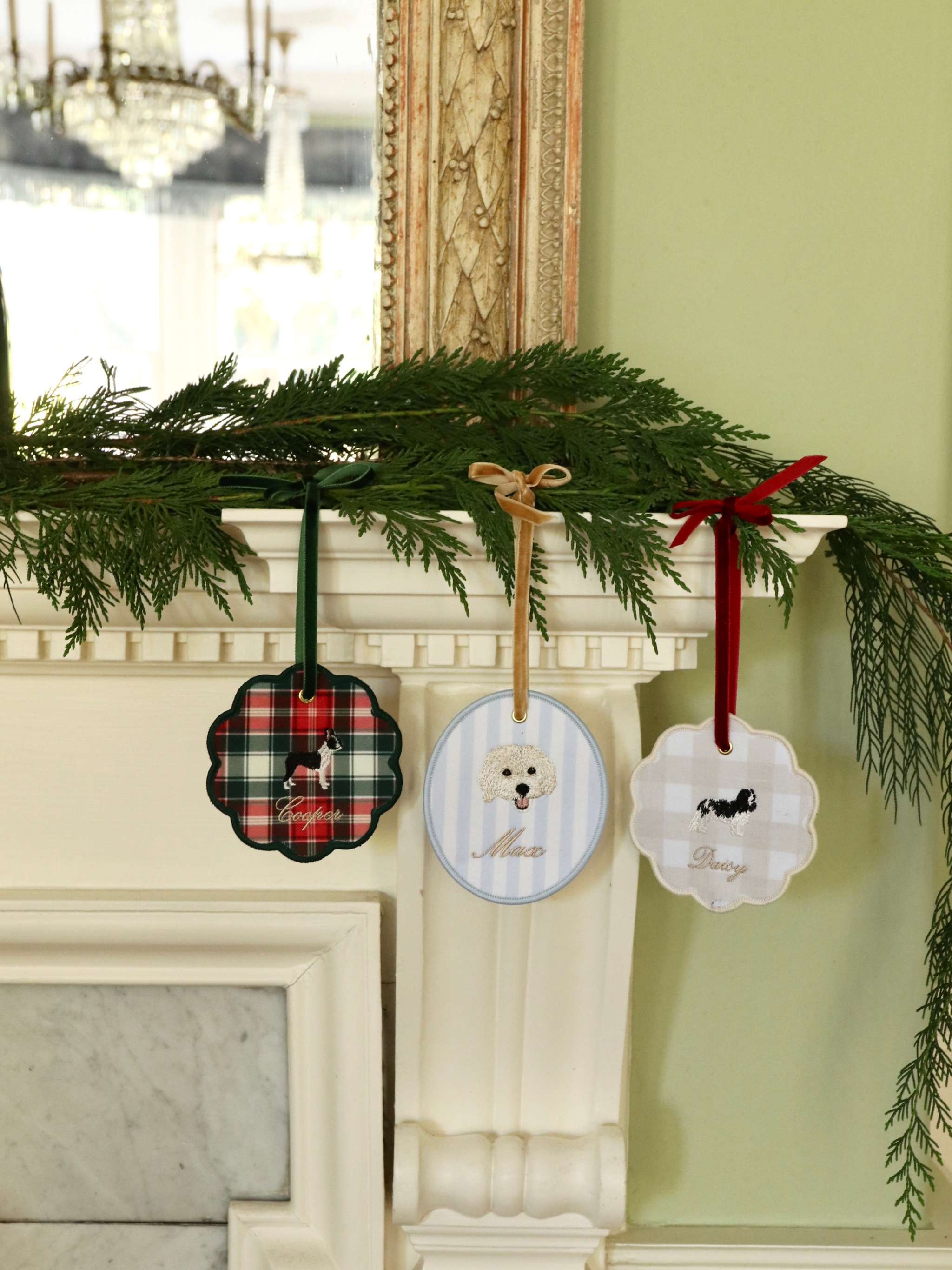 Festive personalized pet ornaments hanging on a decorated mantelpiece with greenery and ribbons