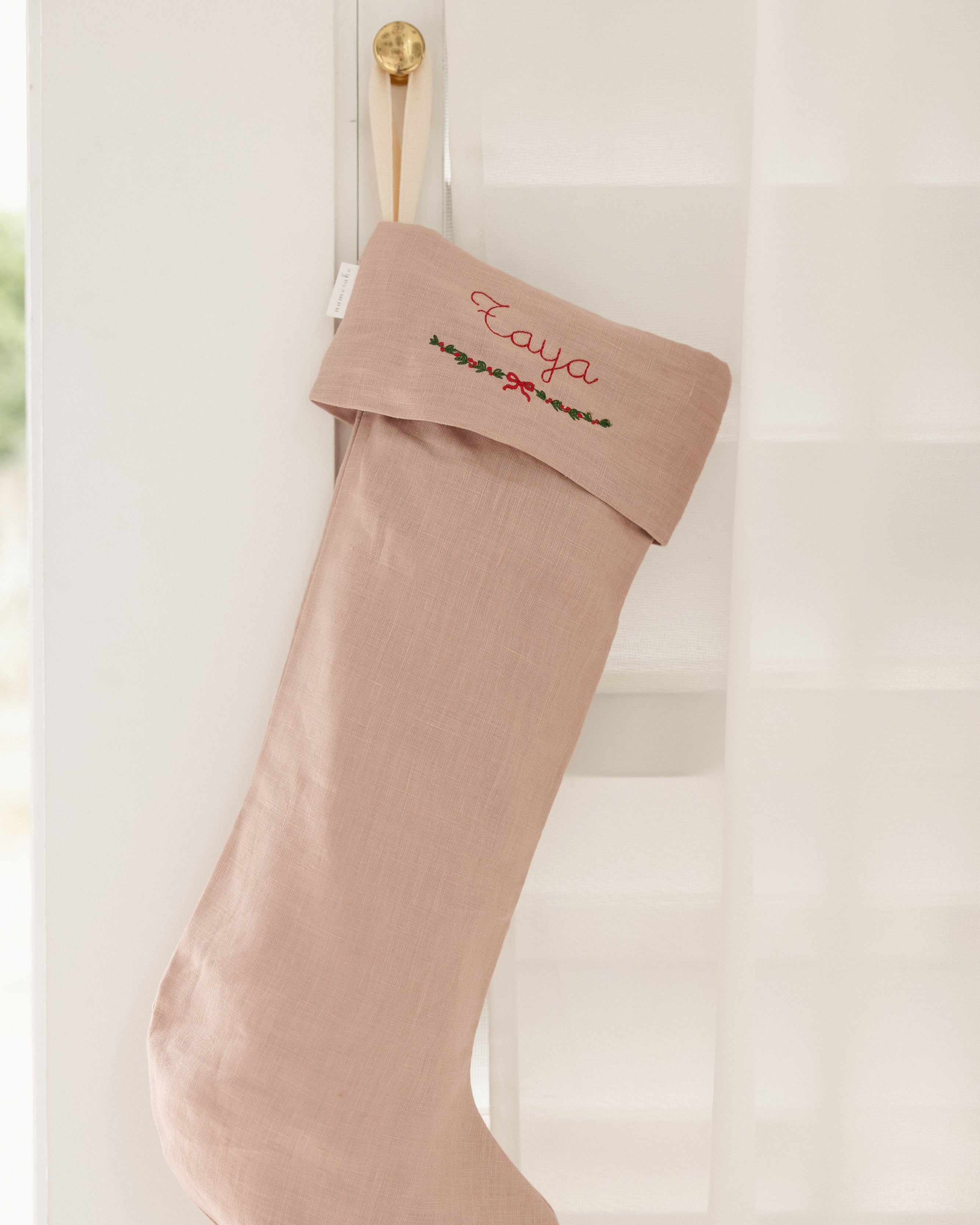 Personalized linen Christmas stocking with red embroidery and festive garland design hanging on white door