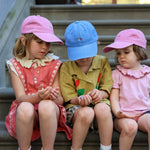 Children wearing personalised hats with multi-coloured text, featuring classic baseball fit and made of 100% washed cotton.