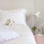 Organic cotton pillowcase with white scalloped edge on a bed.