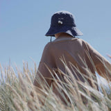 Child wearing navy blue personalised bucket hat with embroidered name and shells detail in outdoor grassy setting