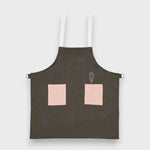 Kids forest green linen apron with pink pockets and adjustable straps.