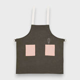 Kids forest green linen apron with pink pockets and adjustable straps.