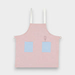 Kids pink linen apron with blue contrasting pockets and adjustable straps, suitable for ages 2-6.